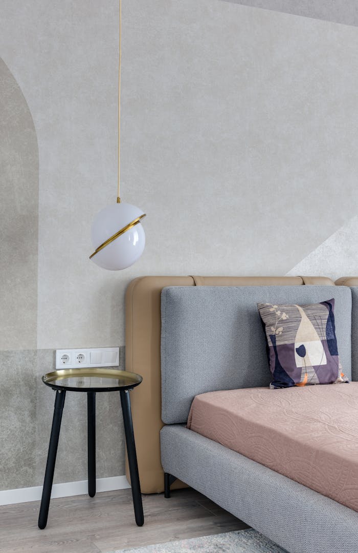 Comfortable bed with colorful pillow near bedside table under lamp with creative design